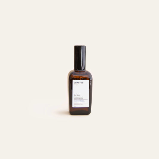 A sleek, amber glass bottle of fragrance sits against a pale green background. The bottle features a black cap and a minimalist label that reads "CHAPTER ORGANICS" and a brief description of the scent.