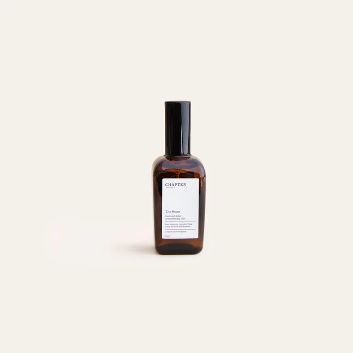 A sleek, amber glass bottle of fragrance sits against a pale green background. The bottle features a black cap and a minimalist label that reads "CHAPTER ORGANICS" and a brief description of the scent.