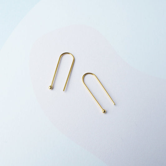 Two gold arch shaped earring on a light grey background