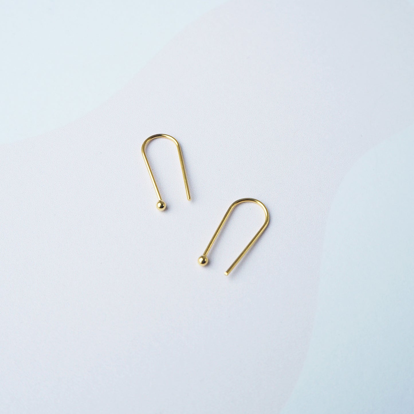 Two gold arch shaped earring on a light grey background