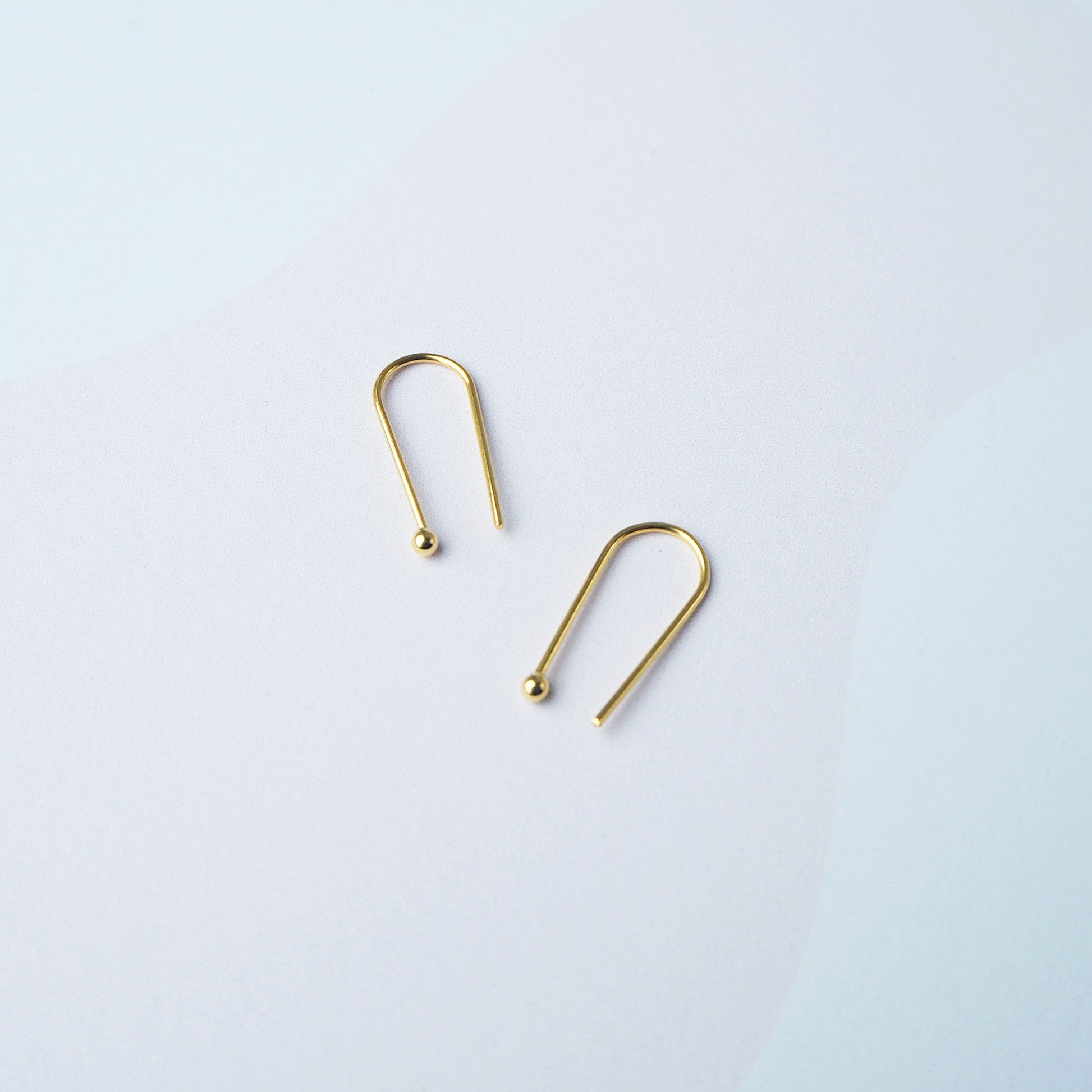 Two gold arch shaped earring on a light grey background