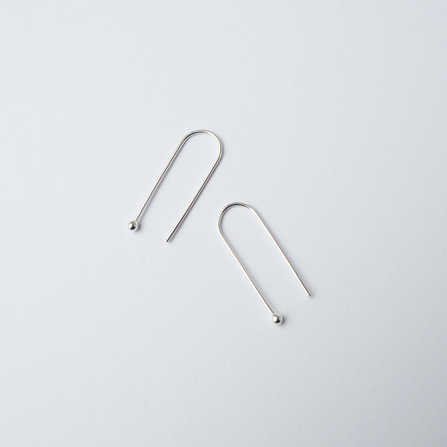 Two silver arch shaped earring on a light grey background