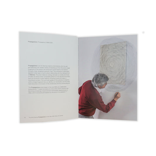 An open spread showing an image of a man in a red jumper drawing onto a wall with pencil on the right-hand-side. On the left is a paragraph of black text on a plain white page.