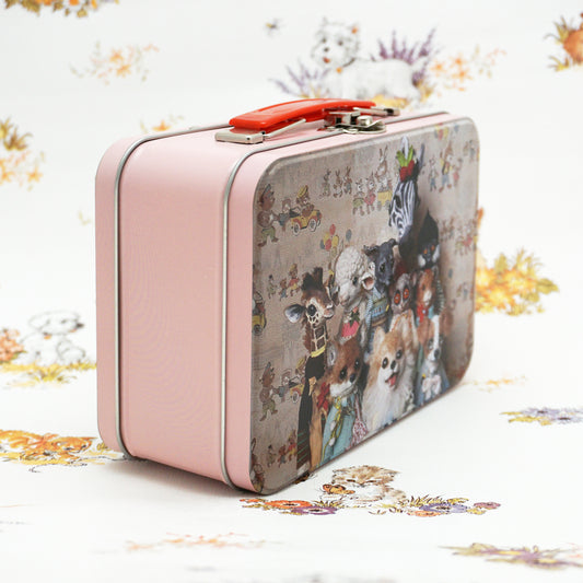 A vintage-style pink metal lunch box featuring a whimsical illustration of various animals dressed in clothes, including a zebra, dog, and lamb. The suitcase is set against a floral-patterned background, adding a playful touch to the scene.