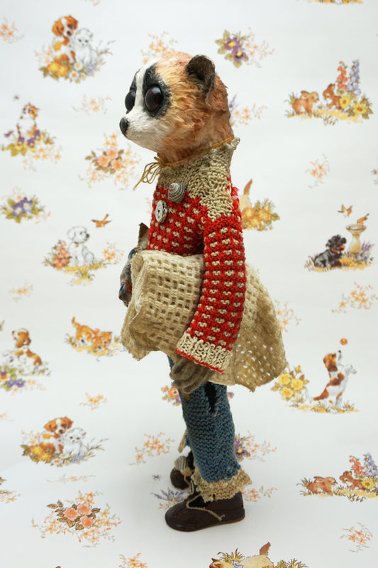 A handmade plush toy of a slow loris dressed in a red knit sweater, blue knit pants, and brown shoes, standing against a white background with a vintage-style animal print.