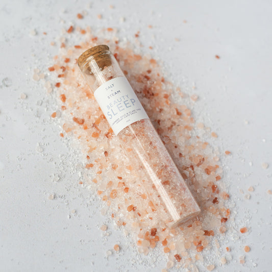 Glass tube filled with pink bath salts on a light gray background