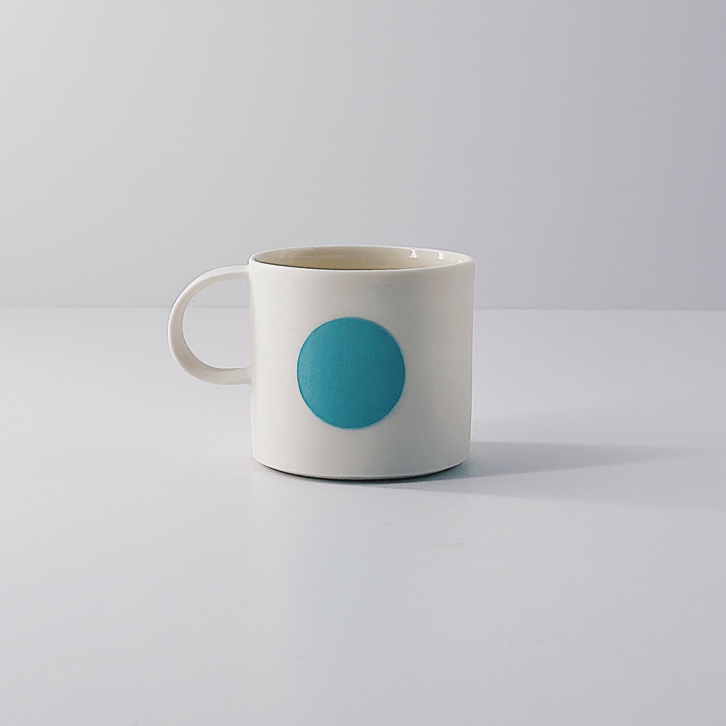 White porcelain espresso mug with a single blue circle on a light grey background