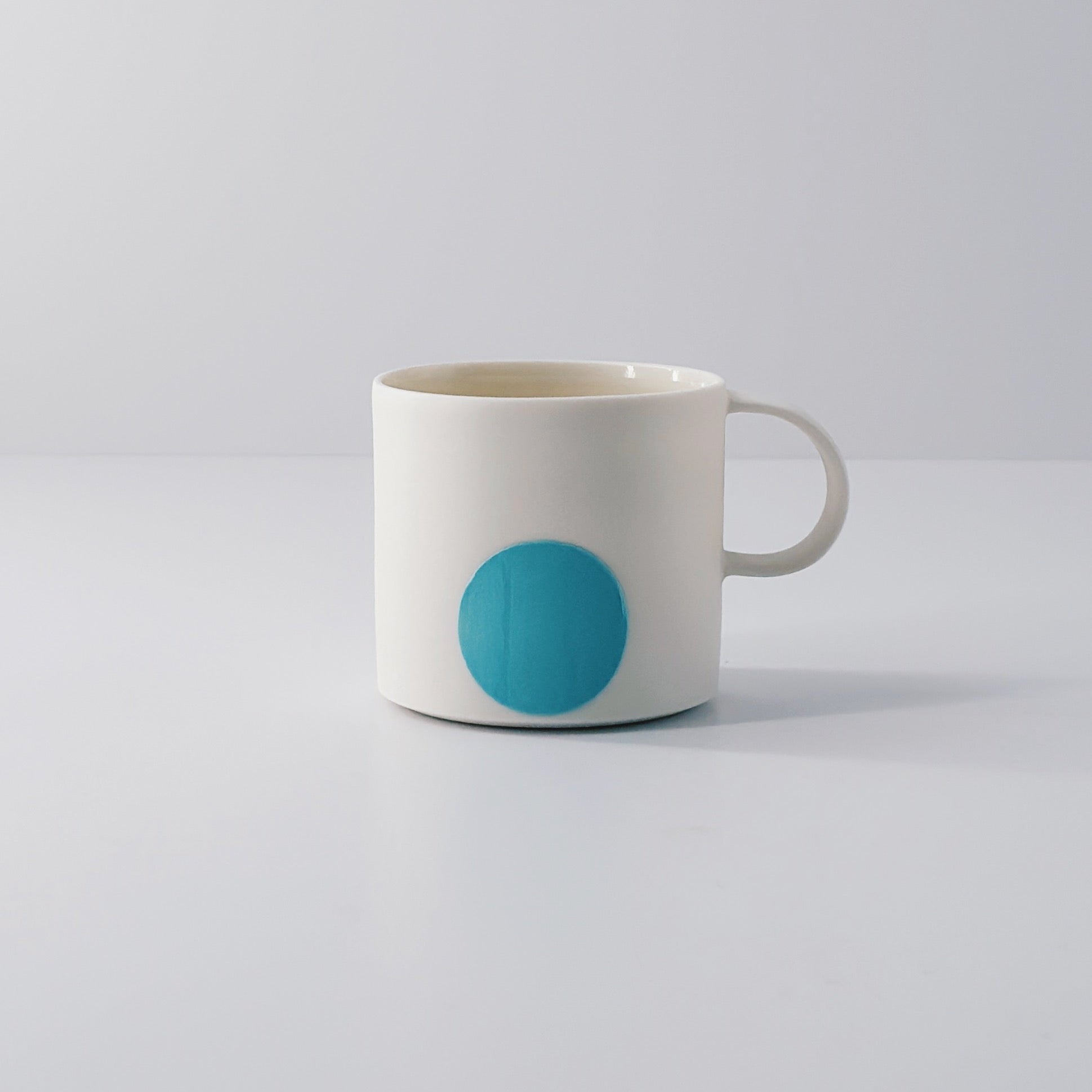 White porcelain espresso mug with a single blue circle on a light grey background