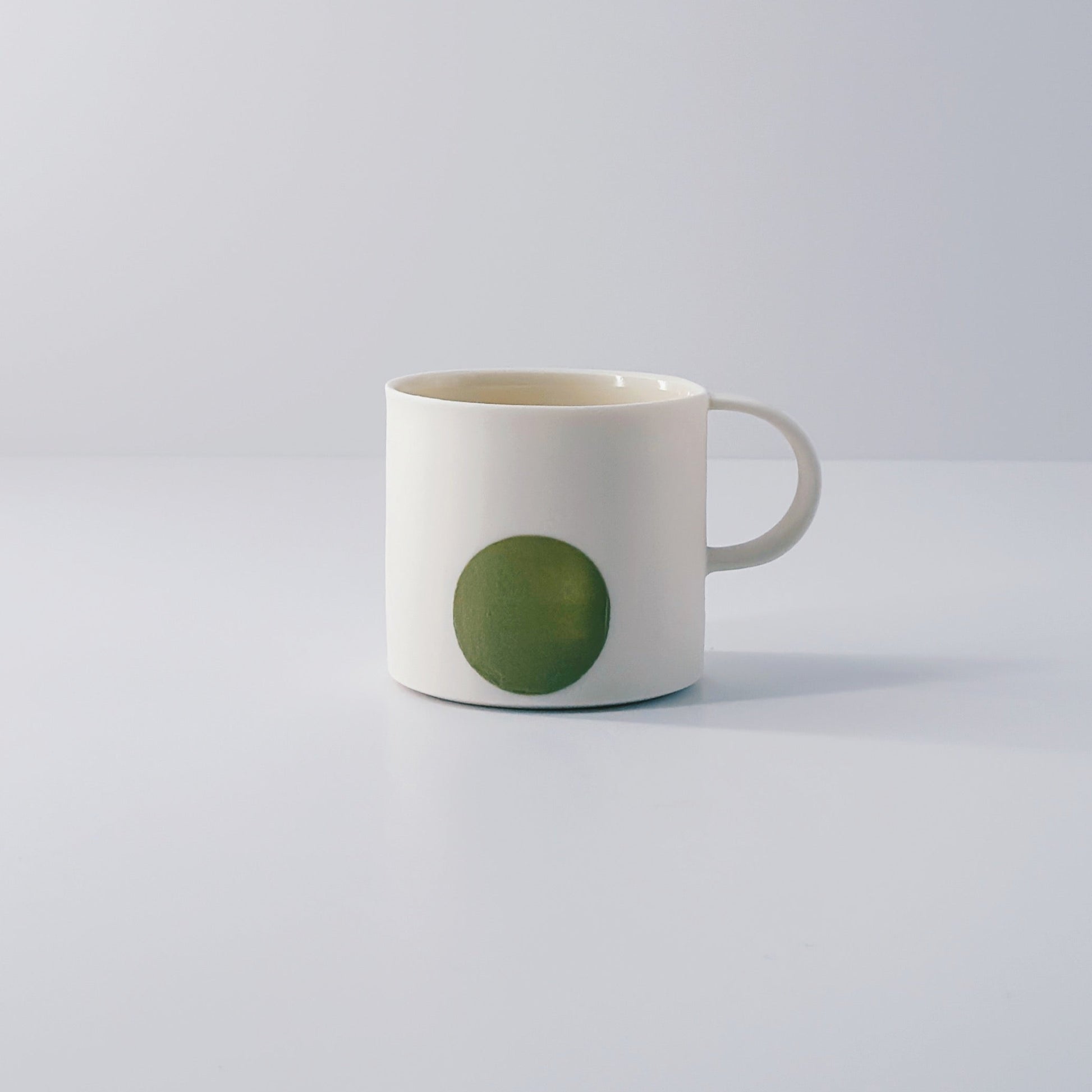 White porcelain espresso mug with a single olive green circle on a light grey background