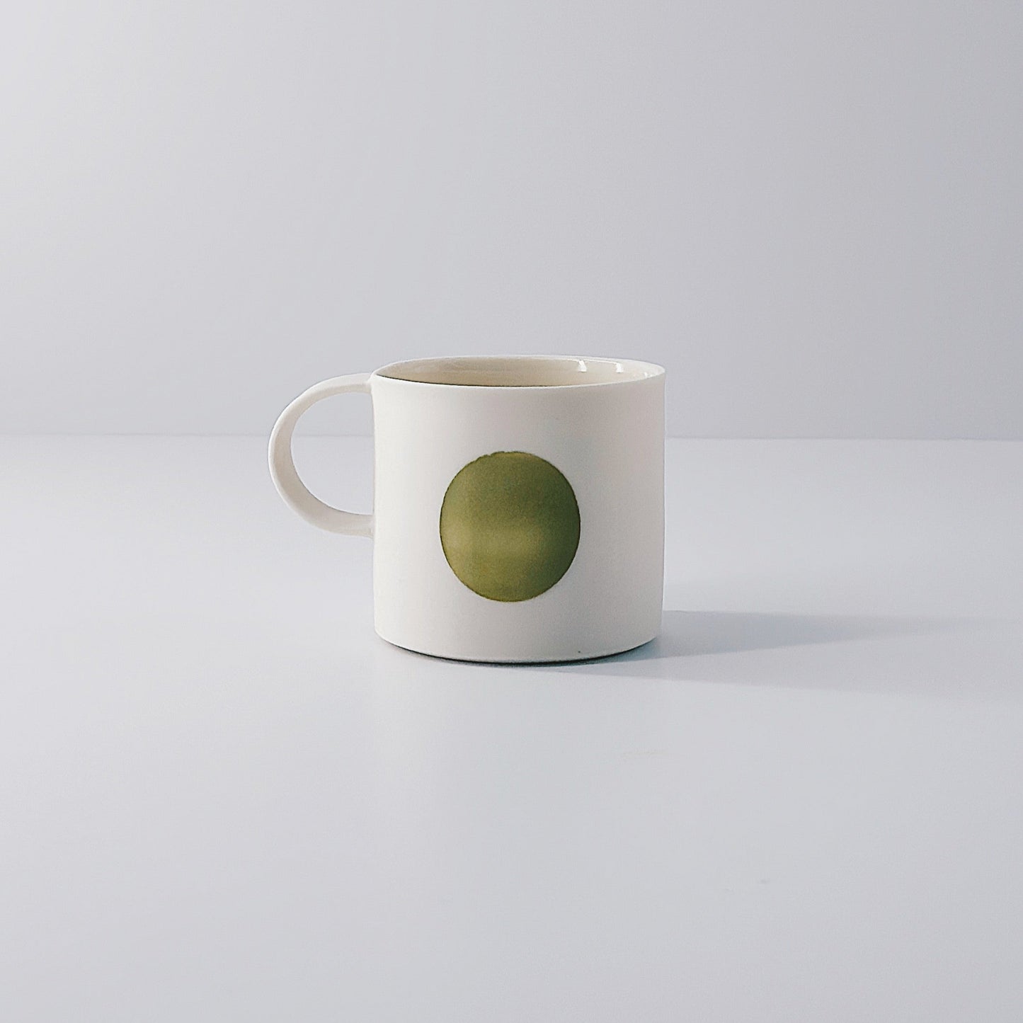 White porcelain espresso mug with a single olive green circle on a light grey background