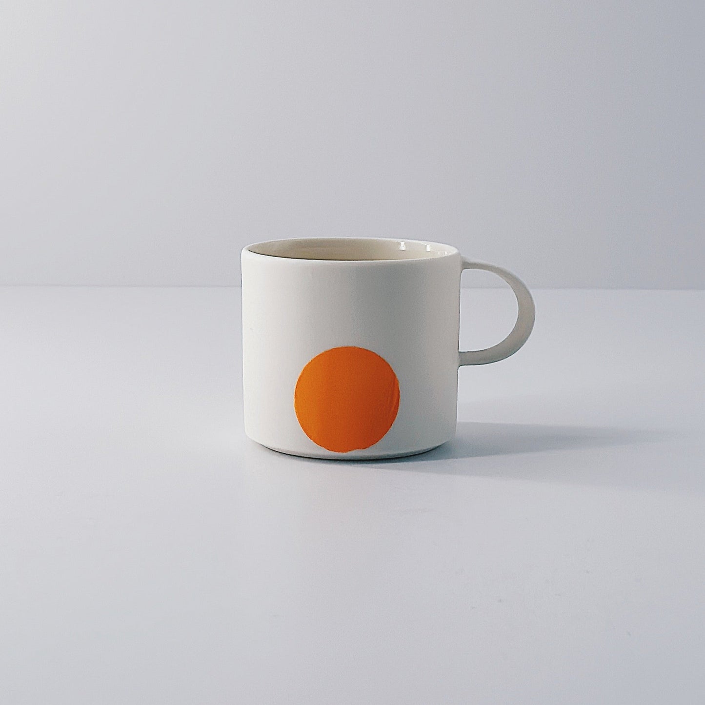 White porcelain espresso mug with a single orange circle on a light grey background