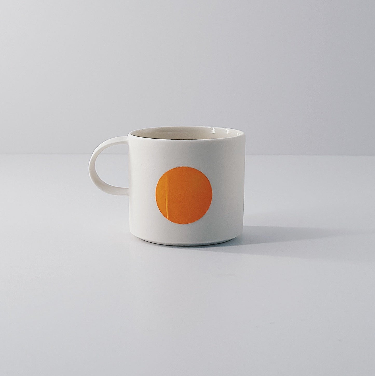 White porcelain espresso mug with a single orange circle on a light grey background
