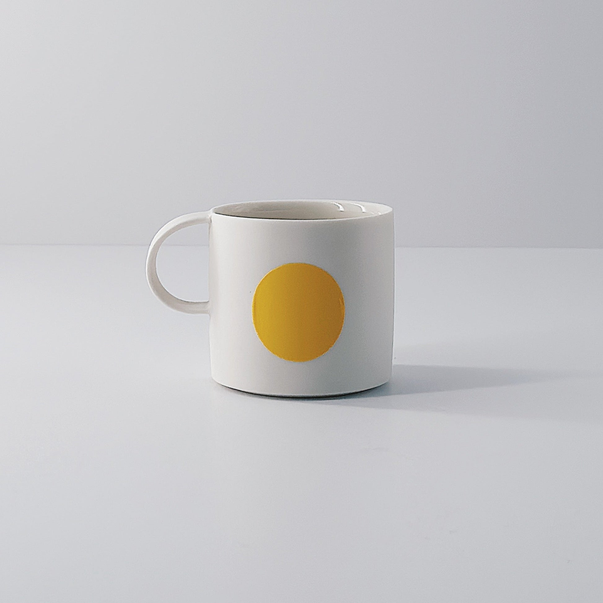 White porcelain espresso mug with a single yellow circle on a light grey background