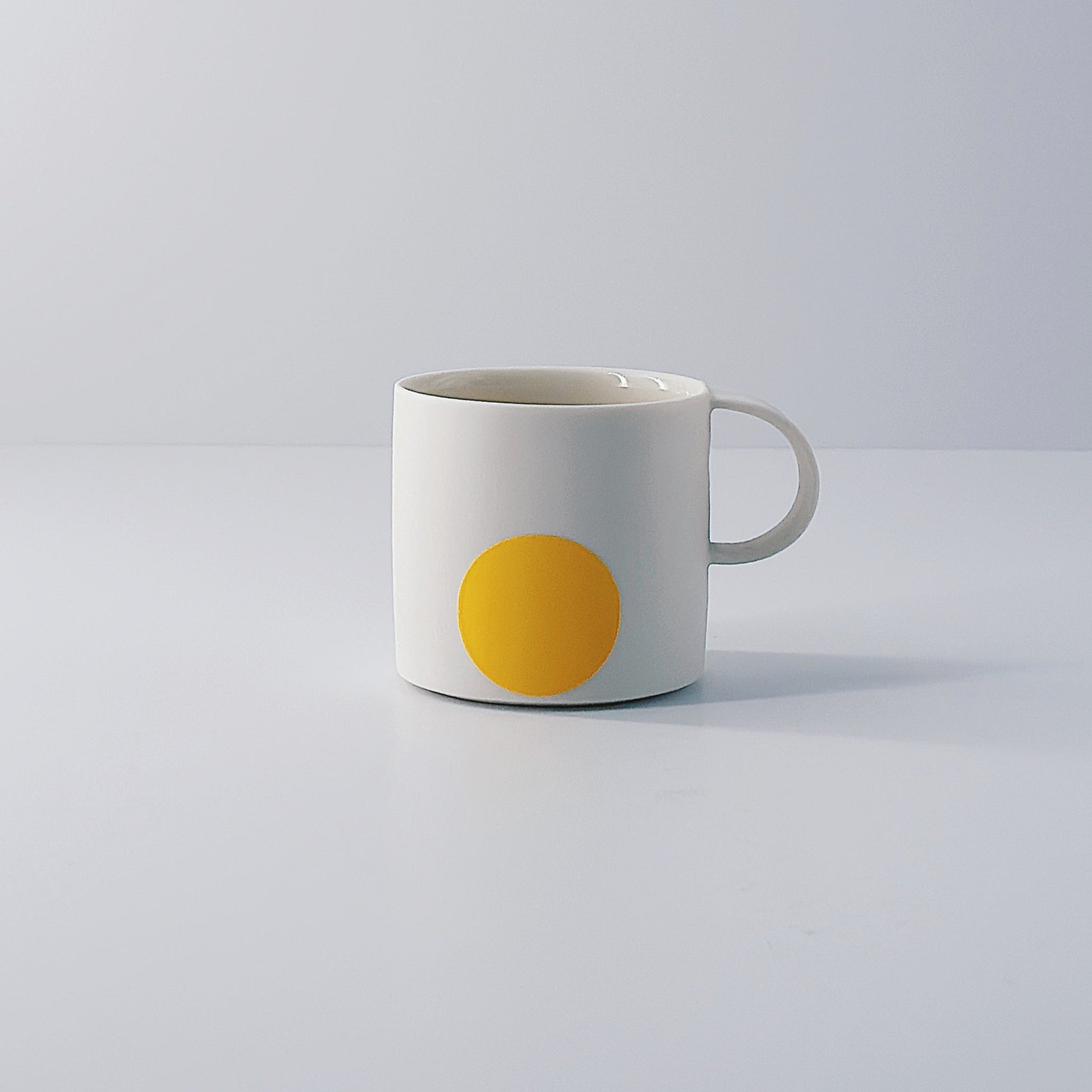 White porcelain espresso mug with a single yellow circle on a light grey background