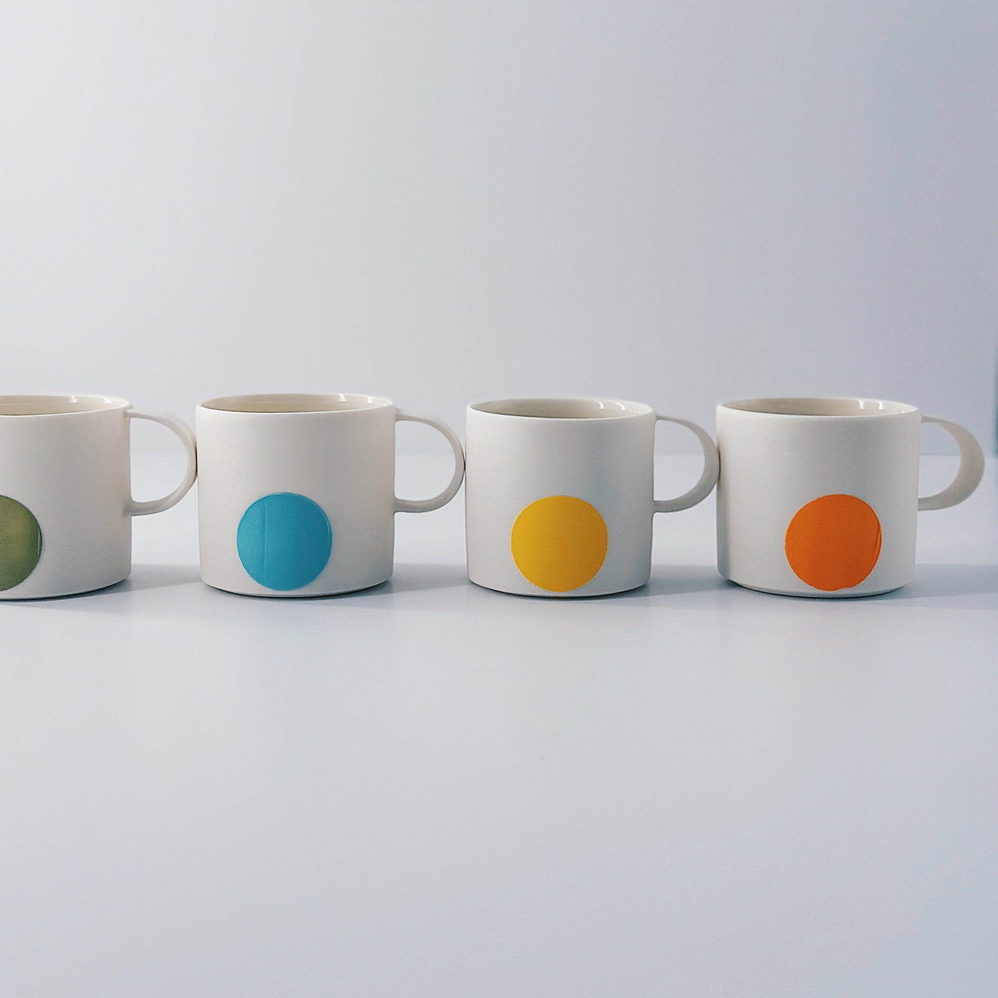 Four white porcelain mugs with coloured dots on a white background