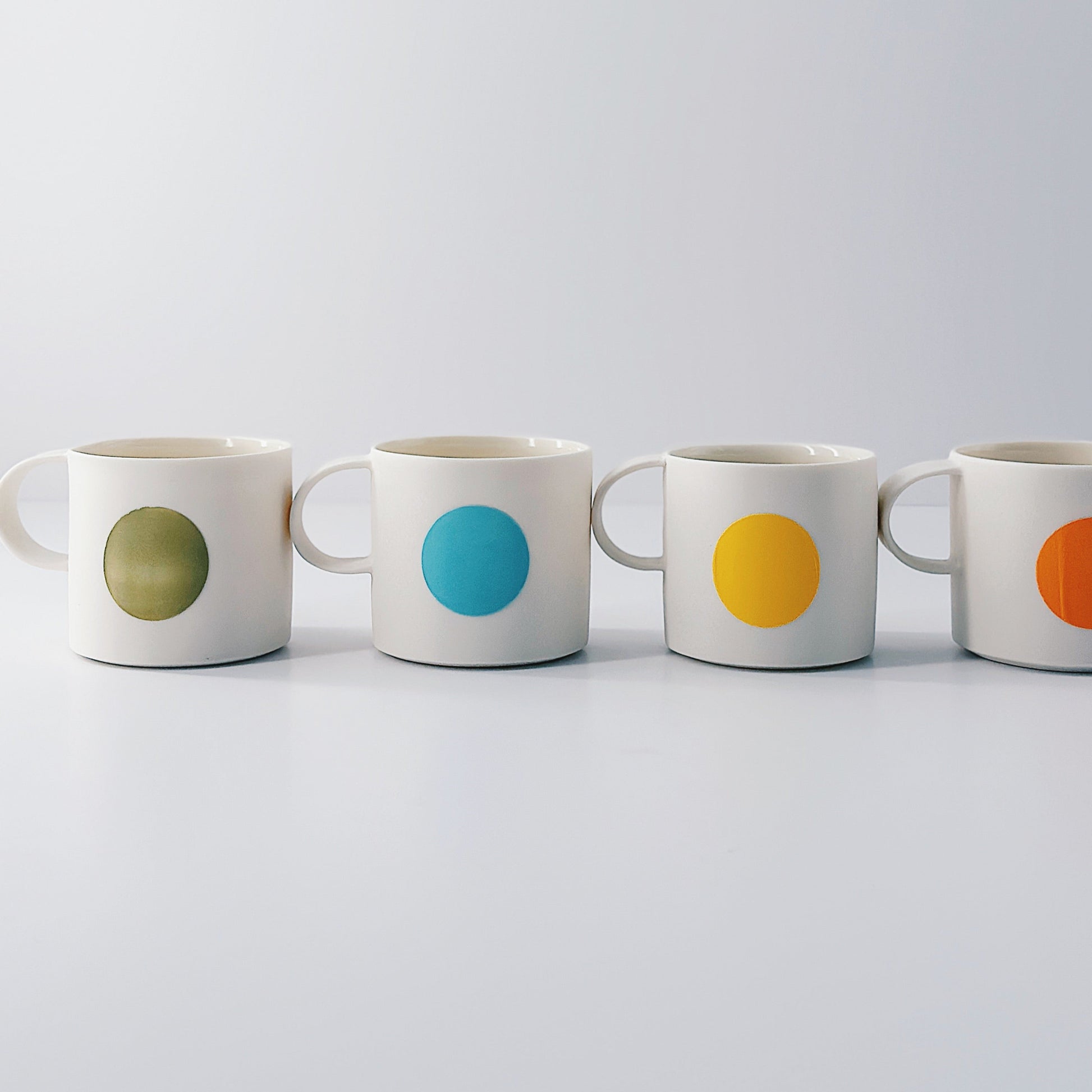 Four mugs with coloured circular designs on a light grey background