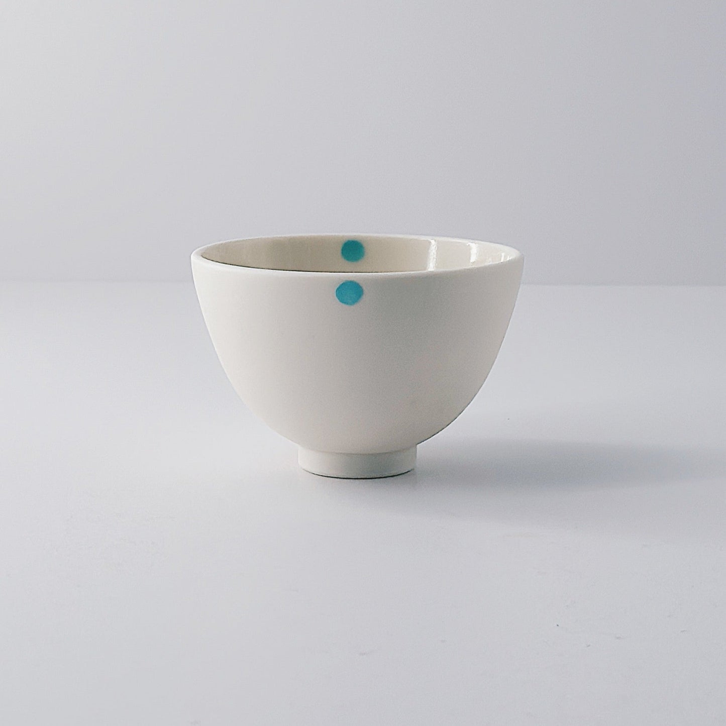 White porcelain bowl with a single blue dot on a light grey background