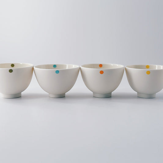 Five small white porcelain bowls each with a single colourful dot arranged in a row on a light grey background