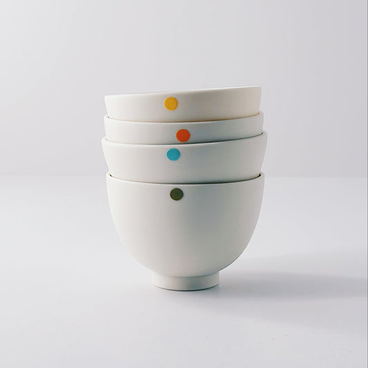 Five small white porcelain bowls each with a single colourful dot arranged in a stack on a light grey background