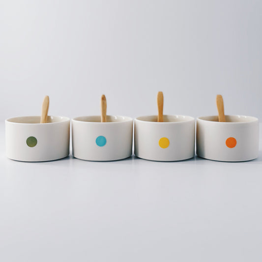 Four small ceramic pots with colourful dot patterns and wooden sticks on a light grey background