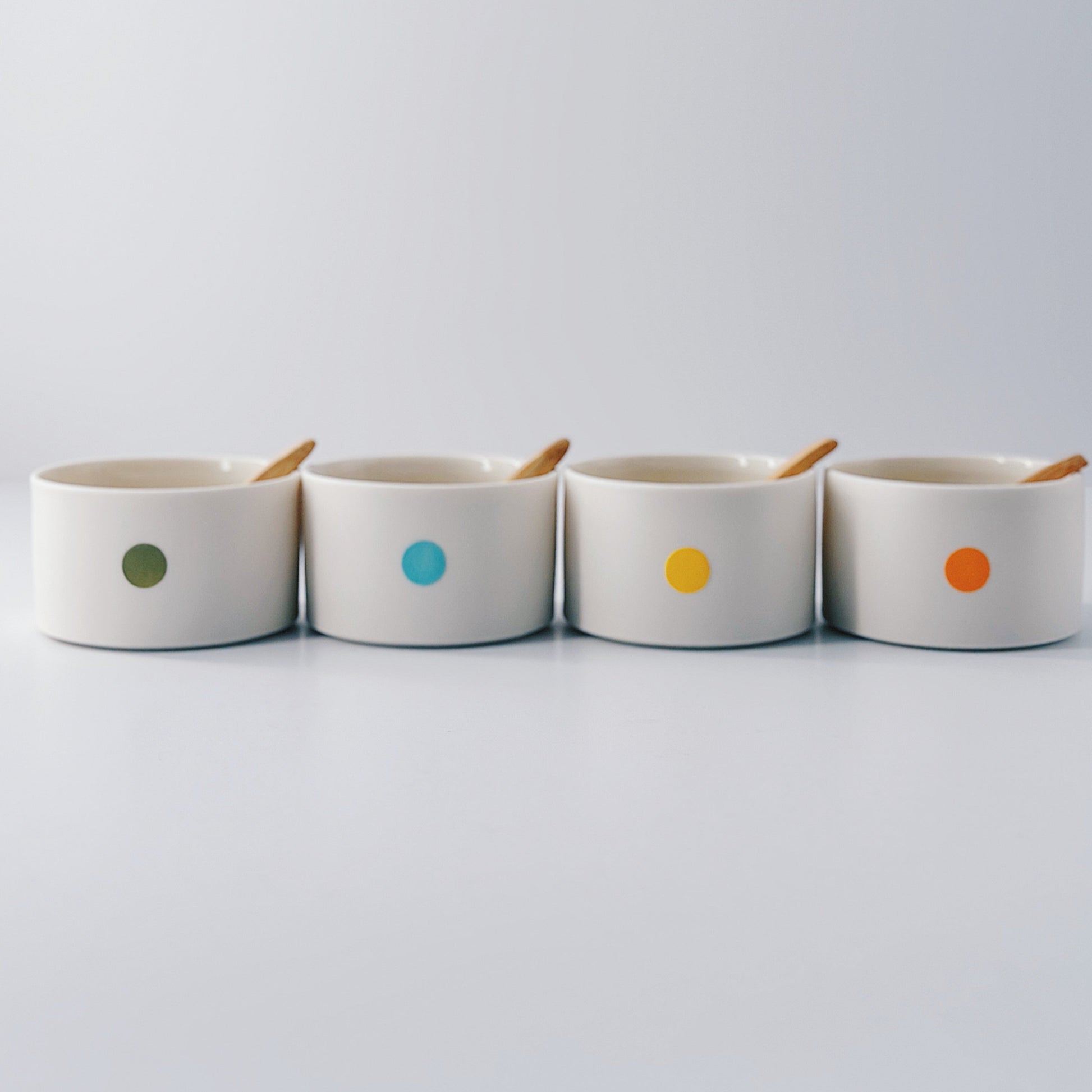 Four ceramic pots with colourful dots and wooden spoons on a light grey background