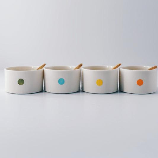 Four ceramic pots with colourful dots and wooden spoons on a light grey background