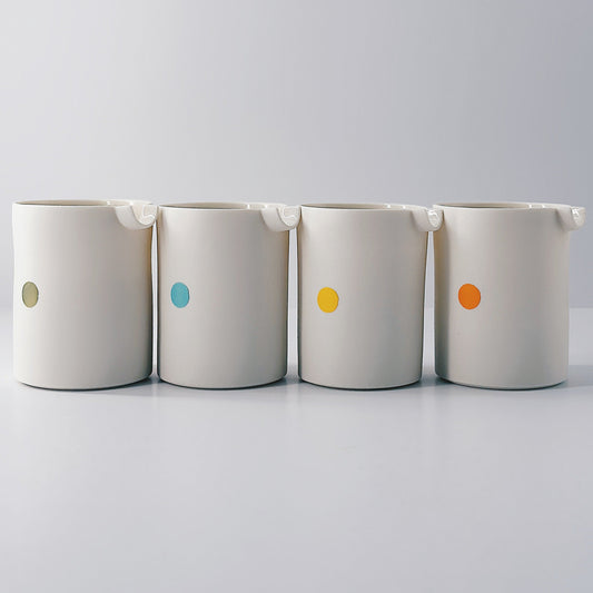 Four white porcelain jugs each with a single coloured dot on a light grey background