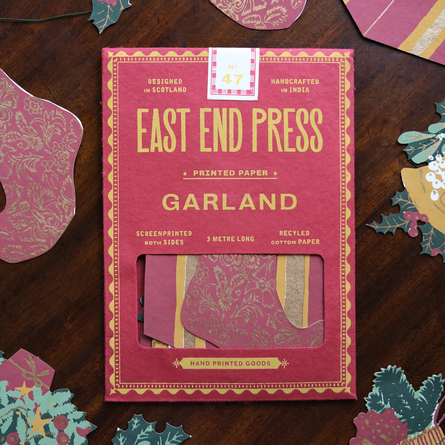 Pink packaging of East End Press Garland on a wooden surface with decorative paper pieces.