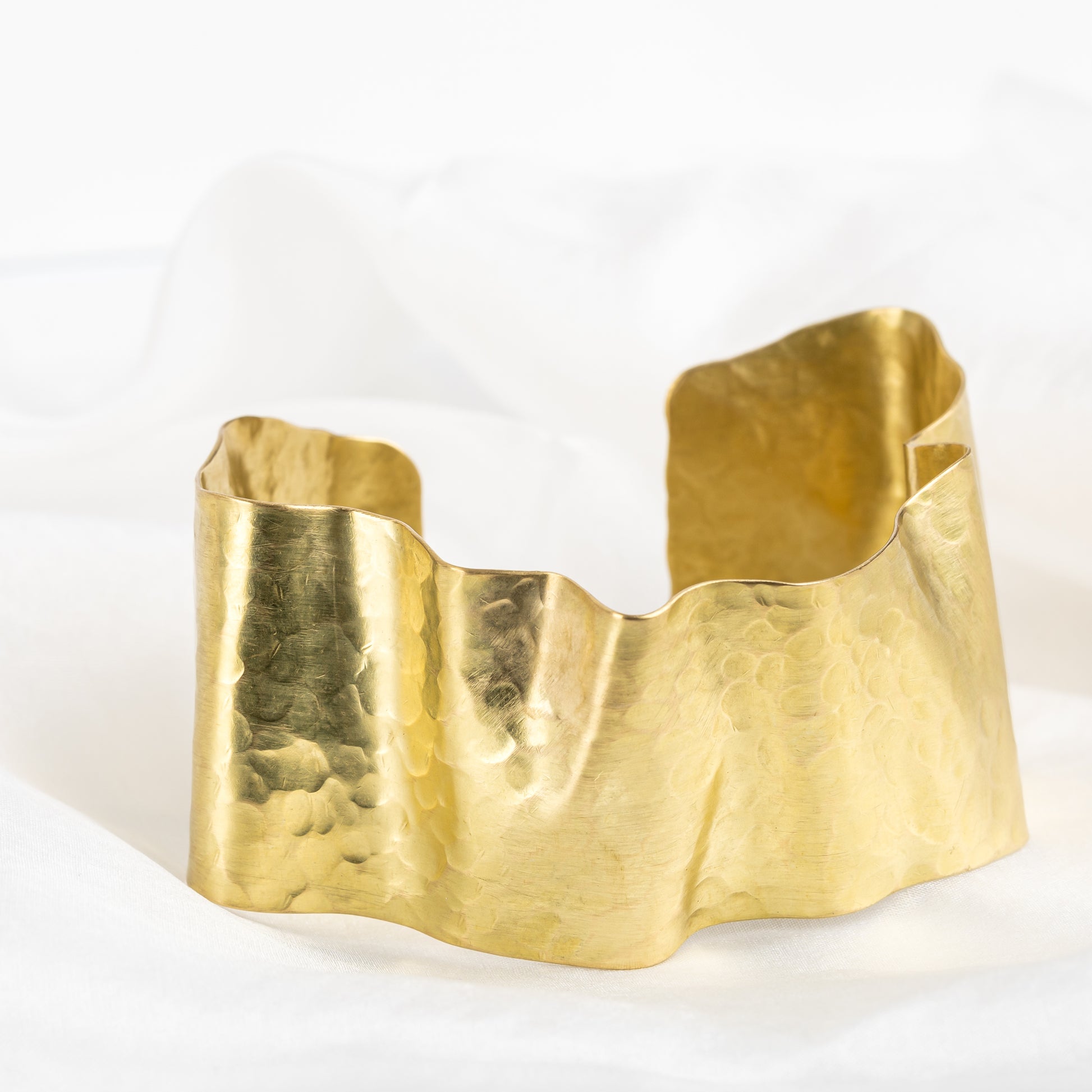 A gold-coloured brass ribbon bangle with a chunky design, displayed on a white background.