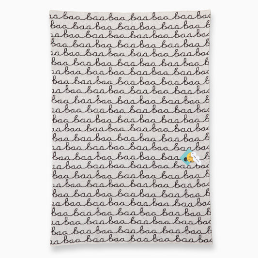 A flat lay of a white and black knitted blanket that features the words Baa Baa and some Donna Wilson swing tags.