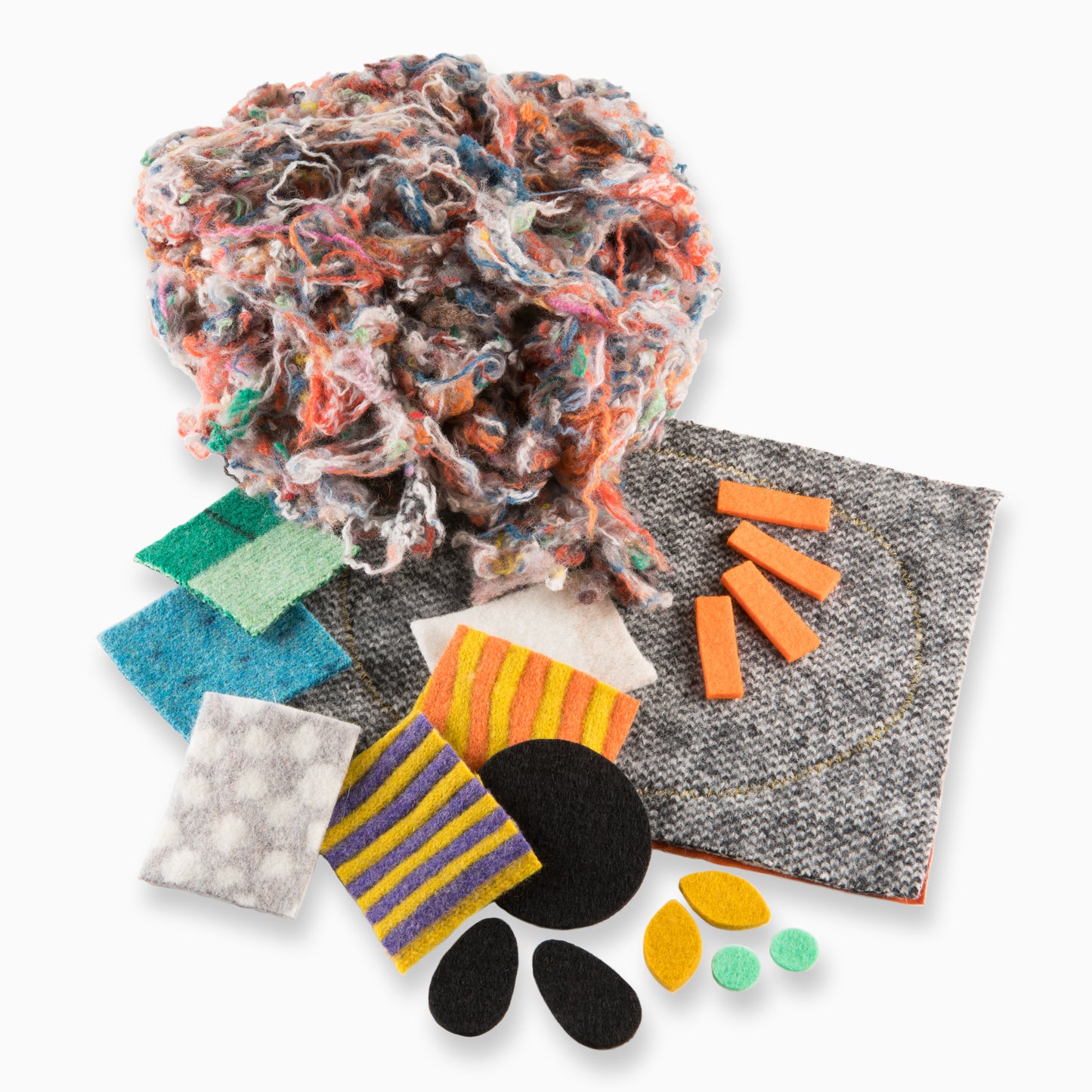 A pile of the contents of the craft kit, including pre-cut colourful shape, larger pieces of wool and colour off-cuts of wool stuffing.