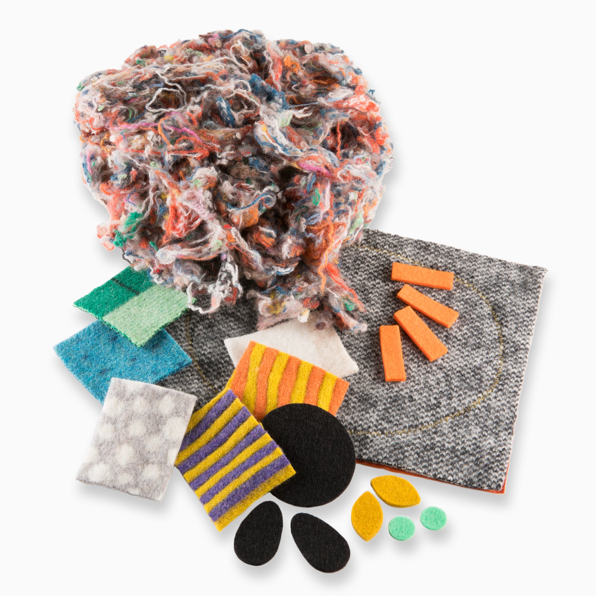 A pile of the contents of the craft kit, including pre-cut colourful shape, larger pieces of wool and colour off-cuts of wool stuffing.