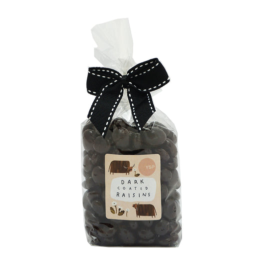 A clear bag of dark coloured coated raisins with a black bow tie. The label is orange and features illustrations of highland cows and flowers.