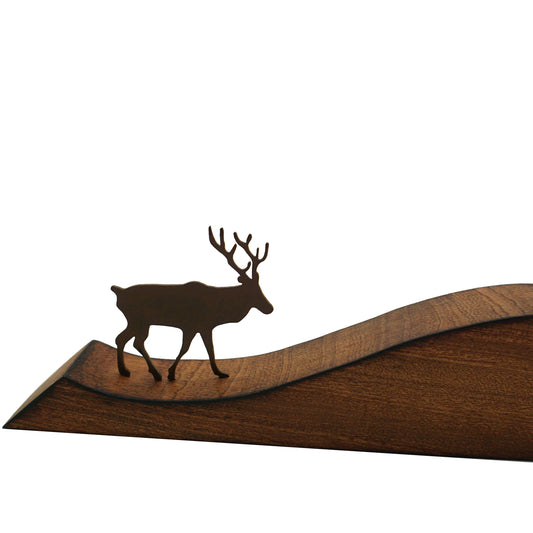 A close up of a laser cut steel stag with antlers on a smooth wooden base.