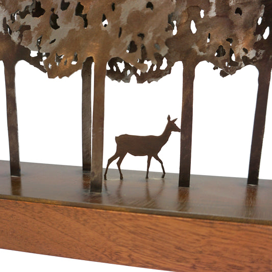 Laser cut metal deer sculpture among tree silhouettes on a wooden base.
