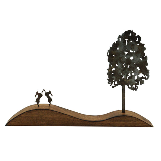 Decorative metal sculpture of two hares dancing under a tree on a wavy base.