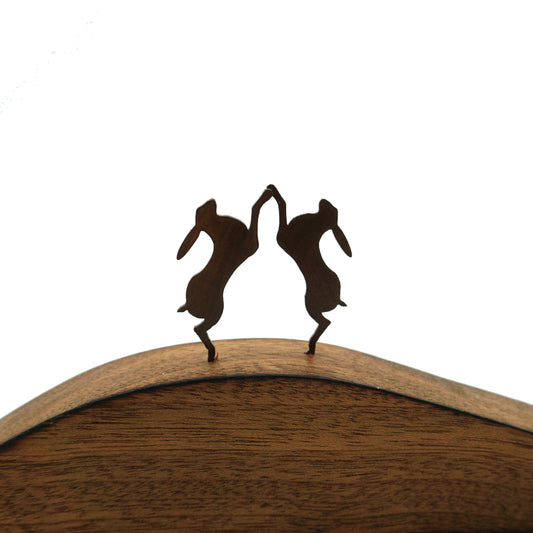 A close up detail of two laser cut hares on a curved wooden base.