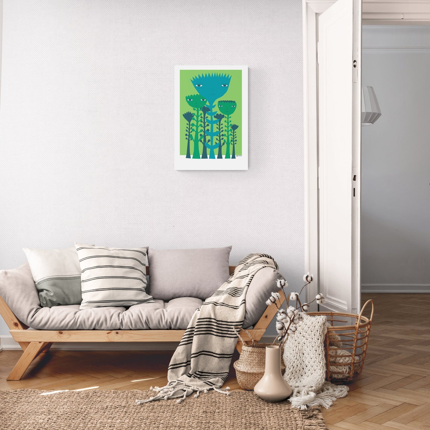 A lounge room with a sofa and blankets showing a screen print with a white border that features green and blue plants and flowers on a small green background hung on the wall to scale.