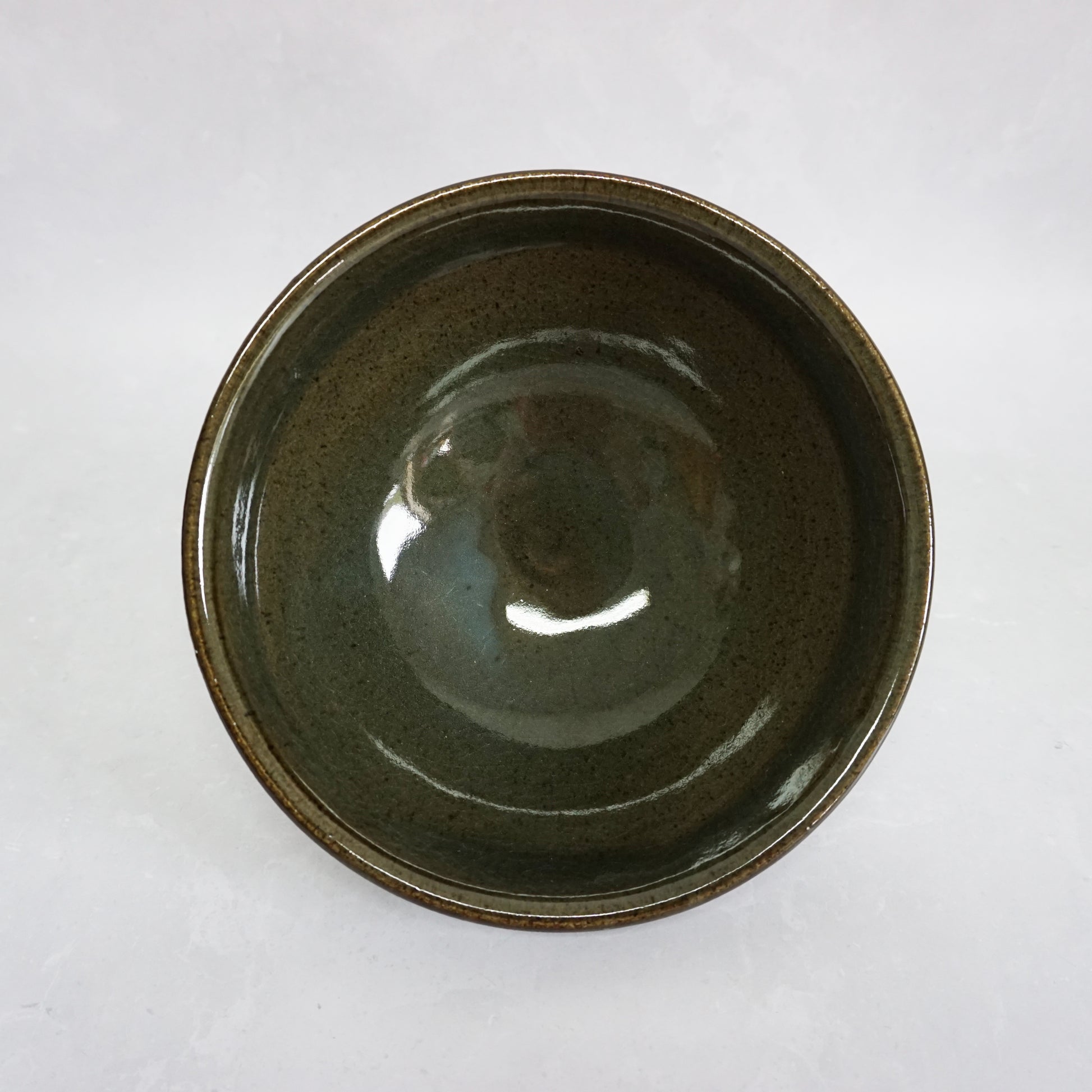 A top view of a large stoneware ceramic ramen bowl with a glaze that has shades of grey and green. The glaze inside is smooth and shiny.