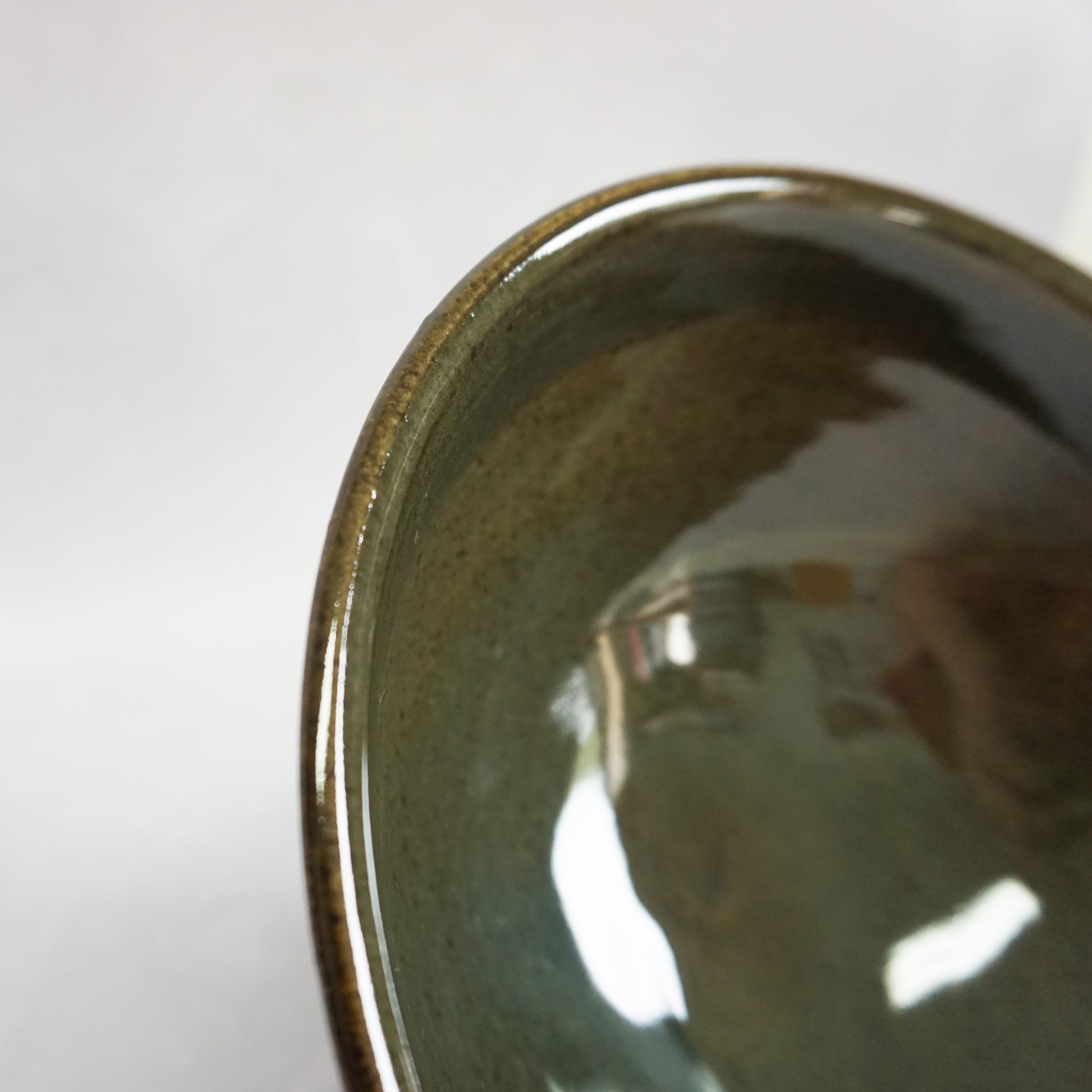 A close up view of the inside of a large stoneware ceramic ramen bowl with a glaze that has shades of grey and green. The glaze inside is smooth and shiny and is reflecting some light.