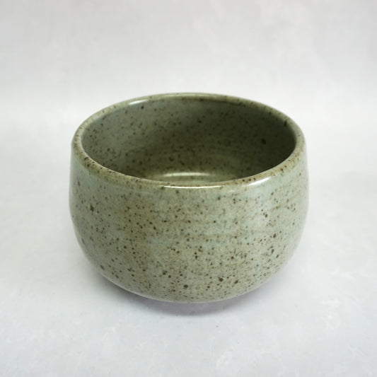 A hand-thrown stoneware ceramic tea bowl with a speckled green glaze.