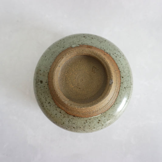 The bottom of a hand-thrown stoneware ceramic tea bowl with a speckled green glaze, featuring the makers stamp.