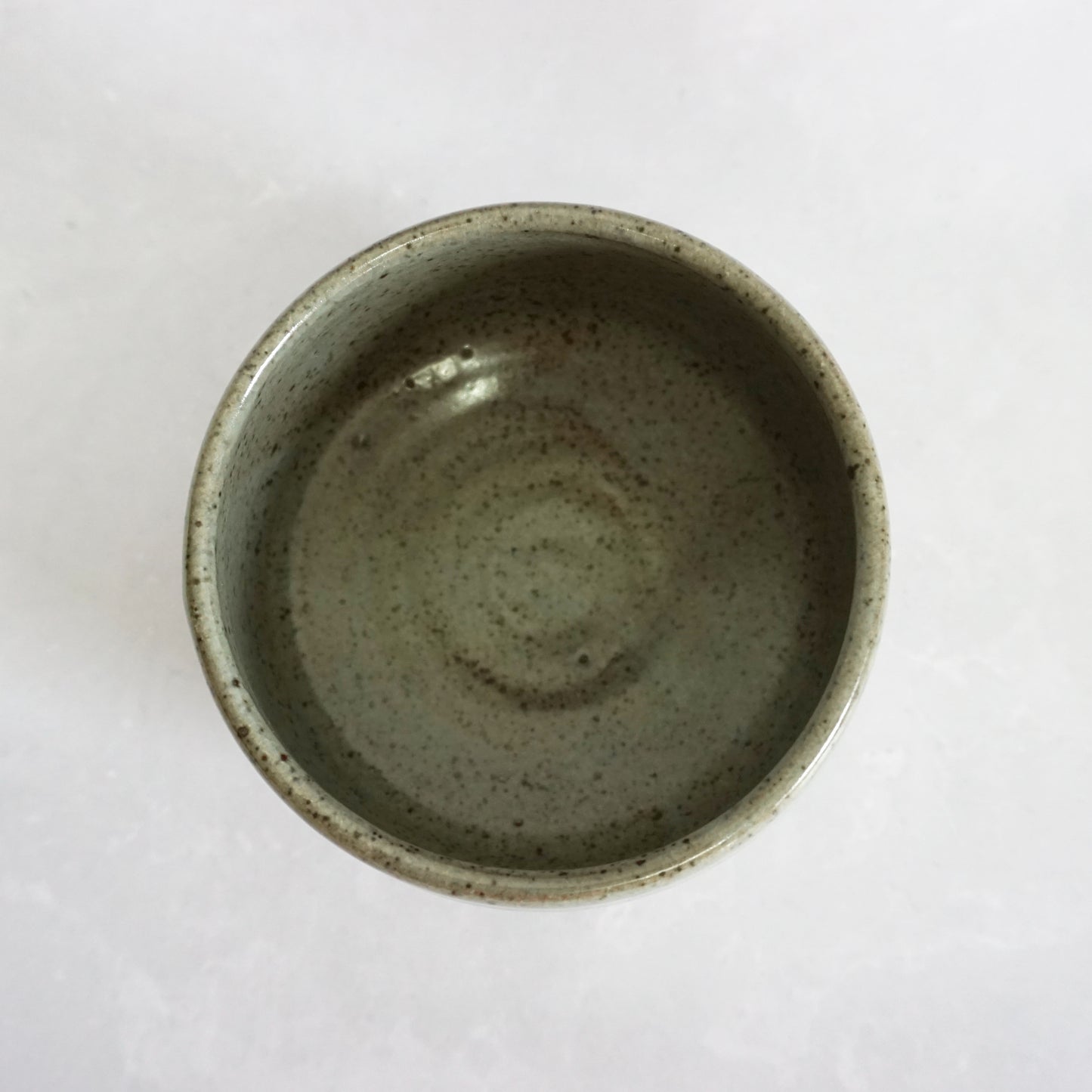 The inside of a hand-thrown stoneware ceramic tea bowl with a speckled green glaze. The inside is smooth and shiny.