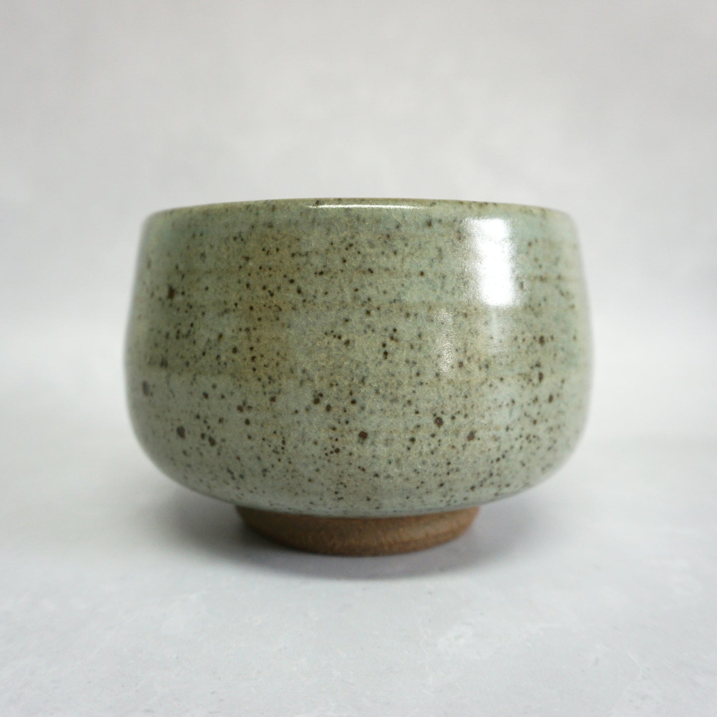 A hand-thrown stoneware ceramic tea bowl with a speckled green glaze.