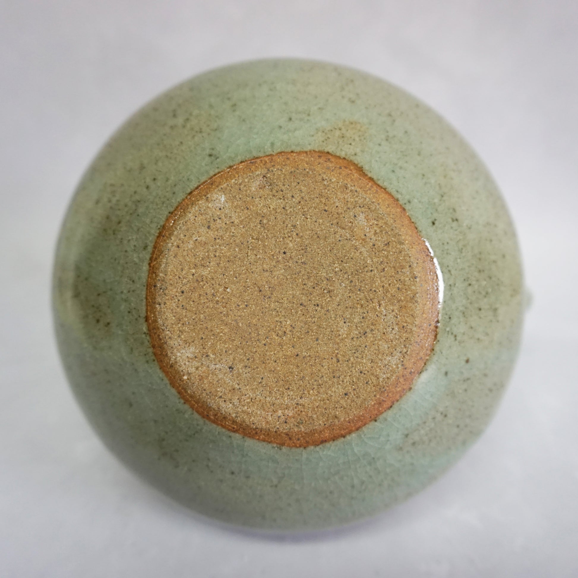 The bottom of a hand-thrown stoneware ceramic teapot with a green glaze. The bottom is brown and unglazed in a circle.