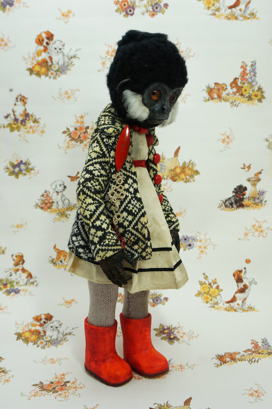 A whimsical doll with a monkey-like face, wearing a patterned coat, white dress, and bright red boots. The background features a vintage-style wallpaper with illustrations of animals and flowers.