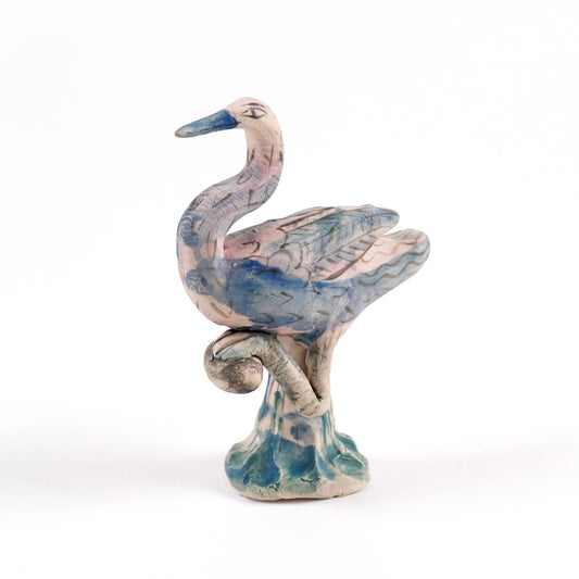A painted ceramic crane whistle in shades of pink and blue on a plain white background.