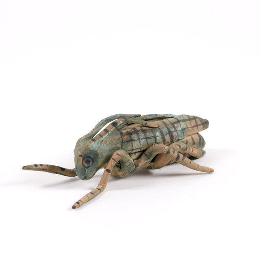 A painted ceramic cricket whistle in shades of green and brown on a plain white background.