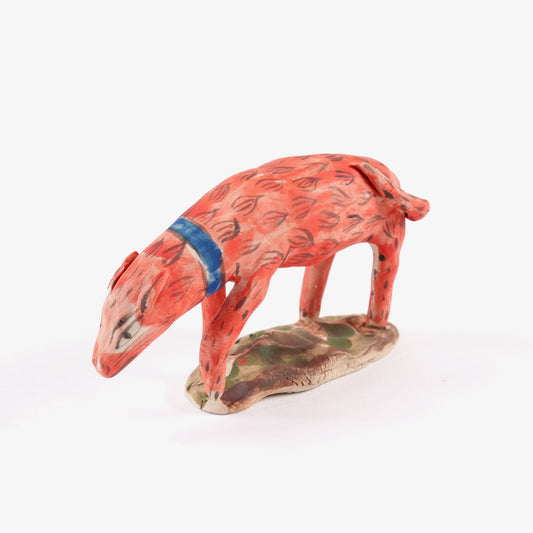 A painted ceramic dog whistle in shades of orange and blue stood on a leafy ceramic base on a plain white background.