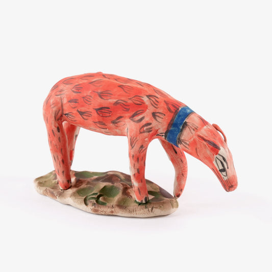 A painted ceramic dog whistle in shades of orange and blue stood on a leafy ceramic base on a plain white background.